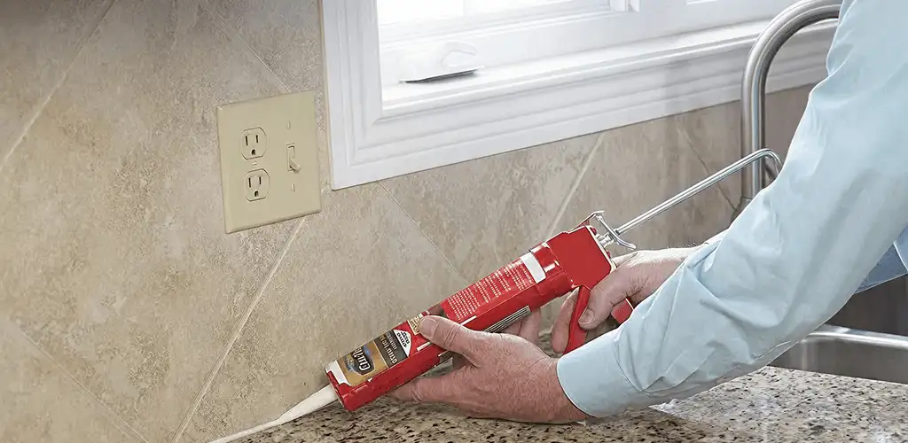 Handyman applying caulk along a kitchen backsplash and countertop seam in Mobile, AL