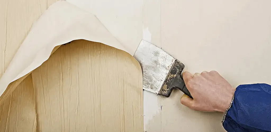 Handyman removing wallpaper with a scraper for wall preparation in Mobile, AL