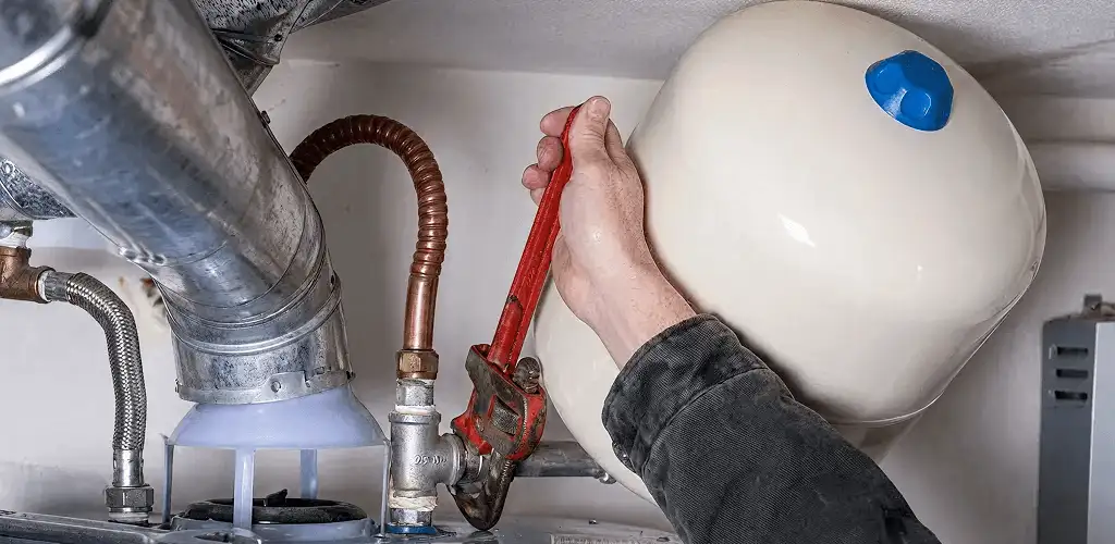 Water heater repair technician tightening plumbing connections near a tank unit in Mobile, AL